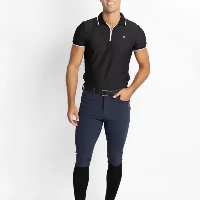 Homem a usar polo preta com gola e mangas com risca branca e calças azuis escuras com meias pretas e sapatilhas brancas