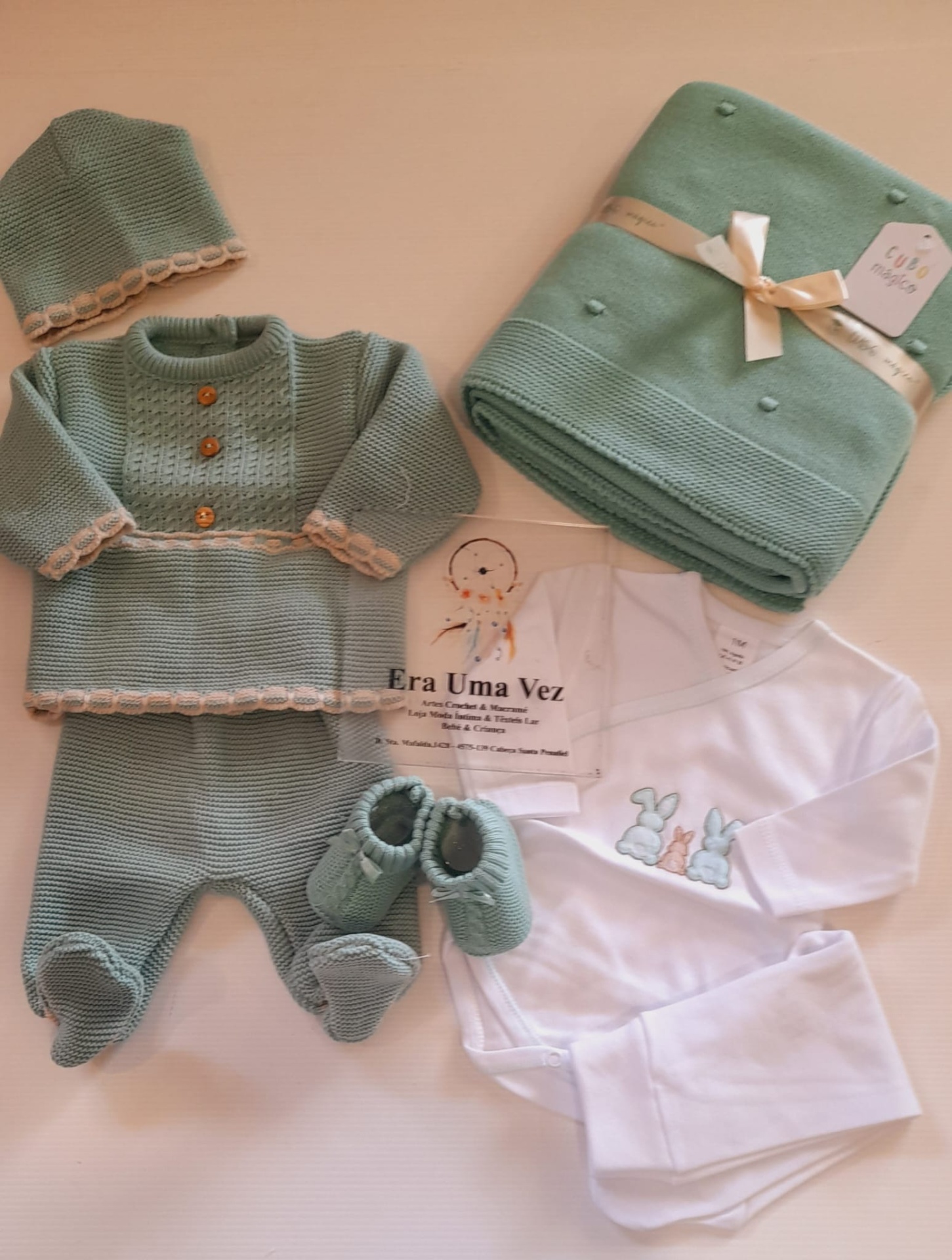 Conjunto de Fatinho e Touca -Outono-Inverno Conjunto roupa bebé malha verde, body branco, manta verde com fita, fundo bege.