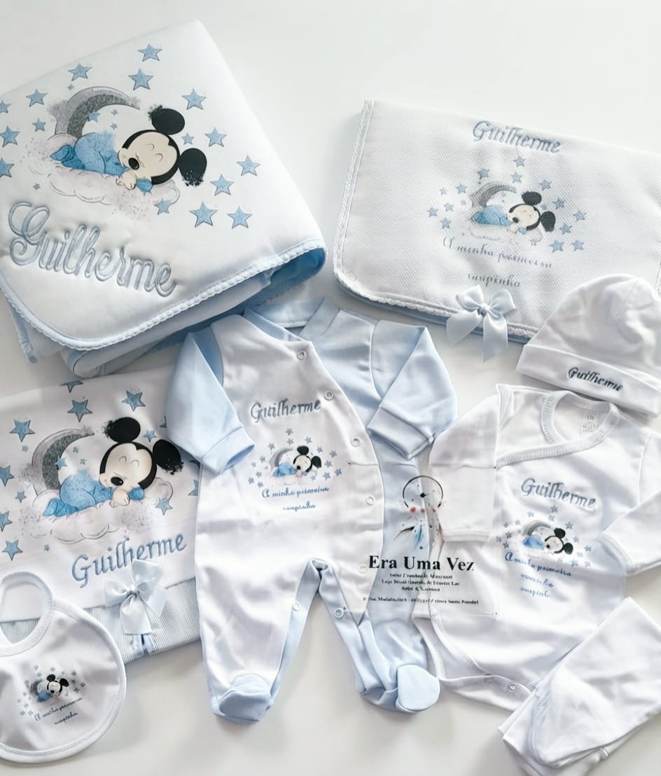 Primeira Roupinha Mickey com Nome Bebé Bordado Conjunto de roupa e acessórios de bebé com personagem Mickey Mouse a dormir, em branco e azul claro.