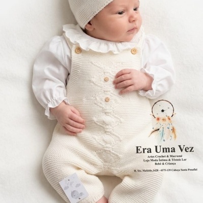 Bebé com roupa branca de malha e chapéu com pompom deitado