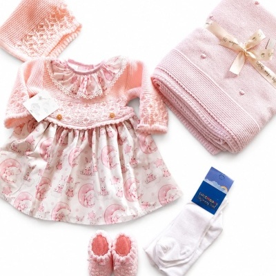 Conjunto de bebé com vestido rosa e estampado de coelhinhos, gorro, sapatinhos, meias e manta.