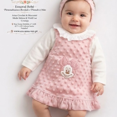 Bebé a usar vestido rosa com padrão bolinhas e bordado Minnie Mouse, com faixa rosa na cabeça.