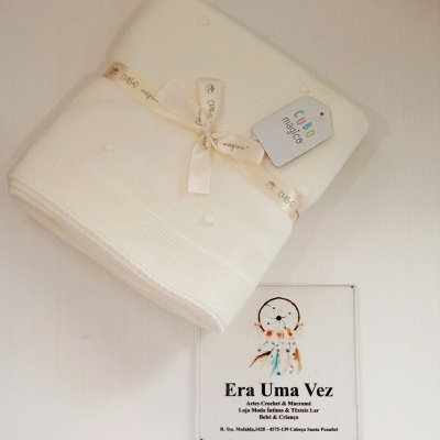 Manta branca de malha com fita e etiqueta CUBO mágico sobre fundo branco com placa decorativa
