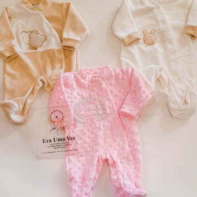 Três pijamas de bebé em veludo bege, branco e rosa com padrões e desenhos bordados.