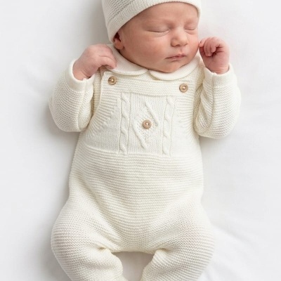 Bebé recém-nascido com macacão e gorro de malha branco creme deitado