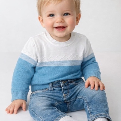 Bebé com camisola branca e azul, calças de ganga e meias brancas sentado em fundo branco.