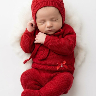 Bebé a dormir vestido com roupa vermelha de malha, sobre fundo branco felpudo