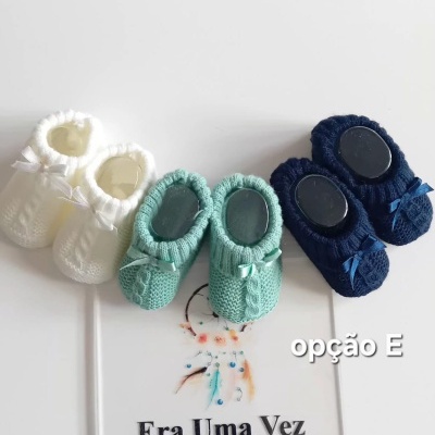 Três pares de sapatinhos de bebé em croché de várias cores sobre cartaz