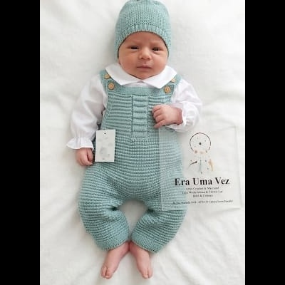 Bebé com roupa de malha azul-pálido e chapéu com pompom em fundo branco com cartão ERA UMA VEZ.