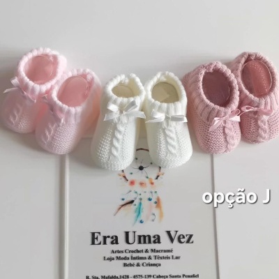 Três pares de sapatinhos de bebé em crochet, dois cor-de-rosa e um branco, sobre folheto com texto
