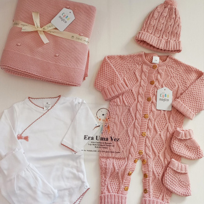Conjunto de bebé com manta, body, casaco, gorro e patucos em tons de rosa e branco.