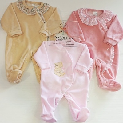 Três macacões de bebé em cores pastel com detalhes florais e bordado, sobre fundo branco.