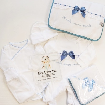 Conjunto de roupa de bebé branca com detalhes em azul e embalagem com laço azul