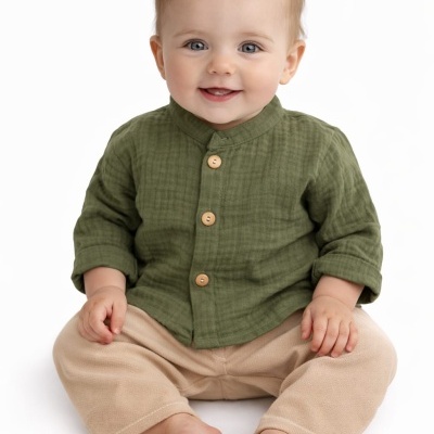 Bebé vestido com camisa verde e calças bege sentado