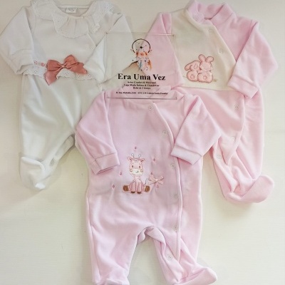 Três macacões de bebé, dois rosa com bordados e um branco com rendas e laço