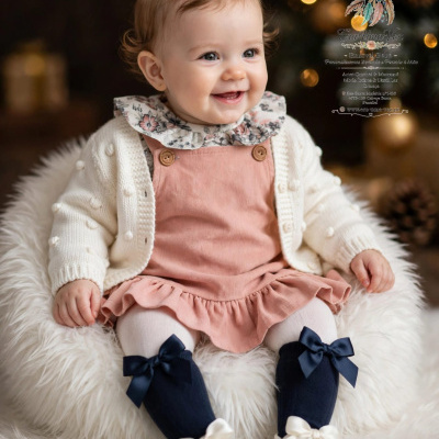 Bebé sorridente com roupa rosa e branca sentado em tecido felpudo branco
