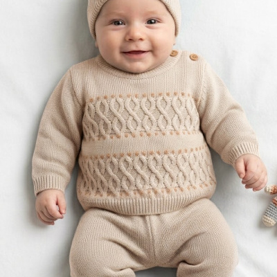 Bebé com roupa de malha bege e gorro com pompom dourado claro sobre superfície branca