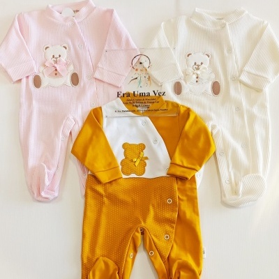 Três macacões de bebé em tons rosa, branco e amarelo com ursinhos e botões de pressão.