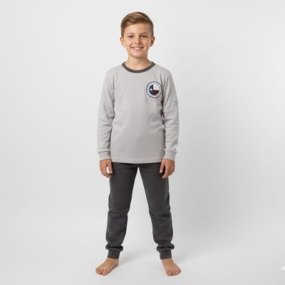 Menino a vestir pijama cinzento com gola escura e emblema no peito, calças cinzentas, em fundo branco