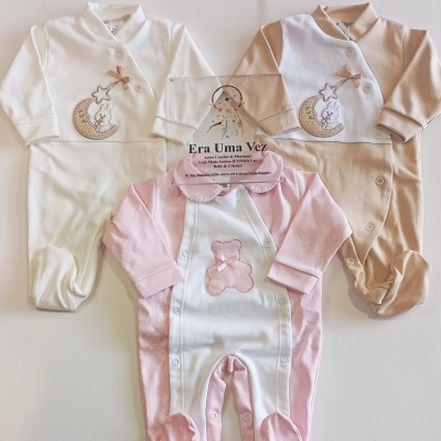 Três macacões de bebé com padrões de coelho, lua e urso em cores branca, bege e rosa.