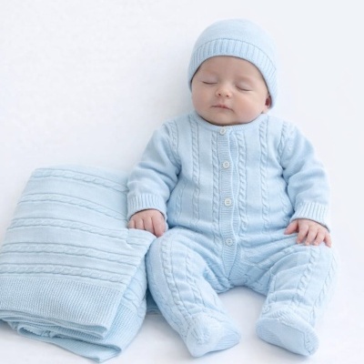 Bebé em fato de malha azul claro com gorro, ao lado de manta da mesma cor