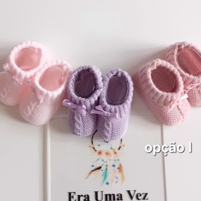 Três pares de sapatinhos de bebé em lã tricotada com laços sobre folheto branco