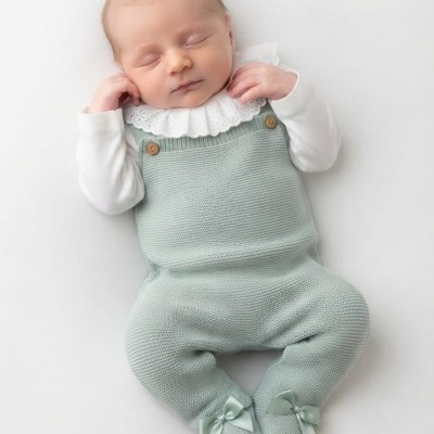 Bebé a dormir de macacão verde-água com botões e camisa branca com gola bordada.
