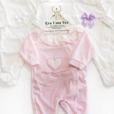 Três macacões de bebé com gola laçada e laços, dourado, branco e rosa, sobre fundo branco.