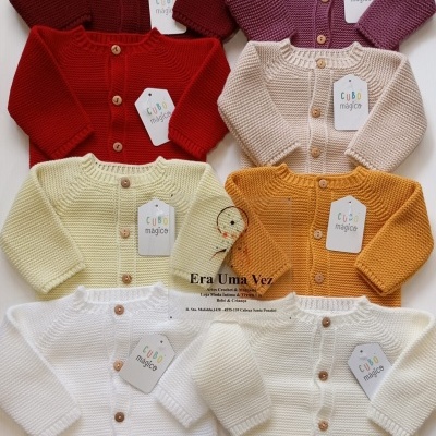 Vários casacos de malha coloridos para bebé com botões de madeira e etiquetas 'CUBO mágico'.