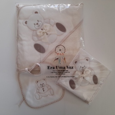 Conjunto para bebé branco e bege com ursinho bordado e laço, composto por toalha, babete e fralda embalados