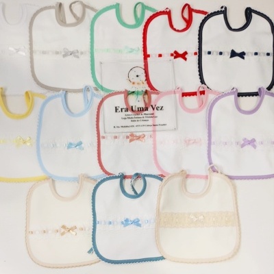 Conjunto colorido de babetes para bebé com bordas e laços variados sobre superfície branca.