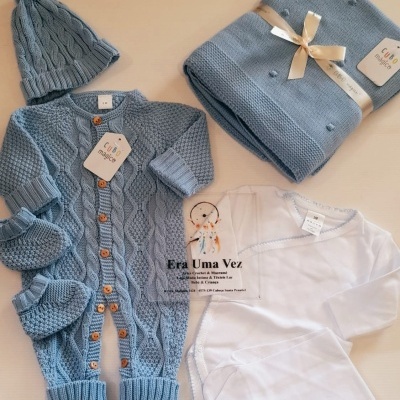 Conjunto de roupa de bebé com peças de malha azul e roupas brancas.