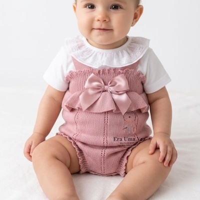 Bebé com roupa rosa e branca sentada sobre fundo branco.