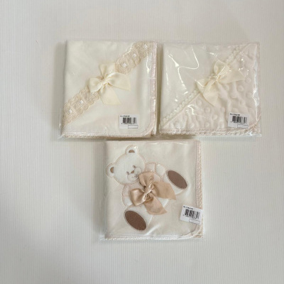 Três mantas de bebê creme com laços e ursinho, embaladas em plástico sobre fundo branco
