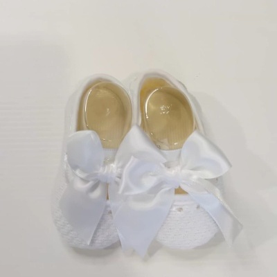 Sapatilhas de bebé brancas com laços de cetim sobre fundo branco