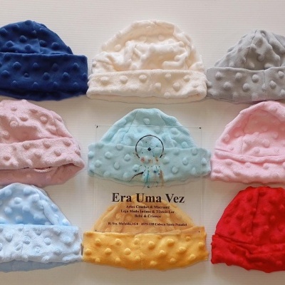 Oito gorros de bebé coloridos em tecido com bolinhas em relevo sobre fundo branco.