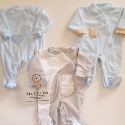 Três macacões para bebé em azul e bege com estampas de coração, coelho e urso.