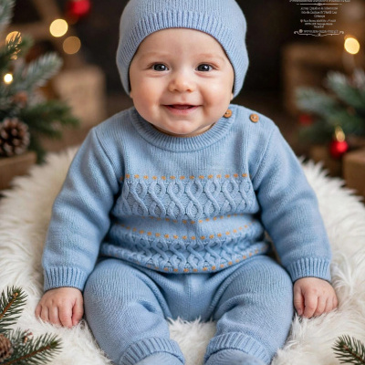 Bebé com fato de malha azul claro e gorro sentado em pelúcia branca com decoração natalícia.