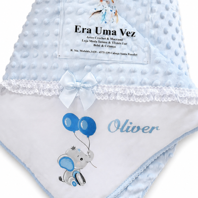 Manta azul bebê com textura de bolinhas, laço azul e elefante com balões e nome Oliver.