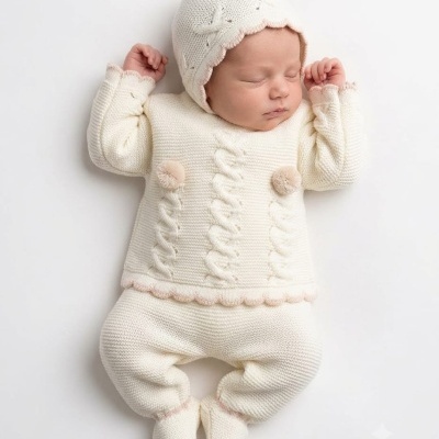 Bebé a dormir vestido com roupa de malha bege clara e rosa pálido