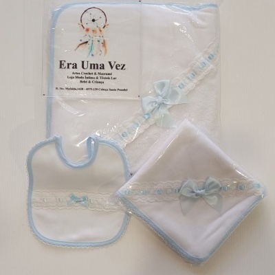 Conjunto de bebé branco com acabamento azul e renda, incluindo babete, toalha e fralda embalados em plástico