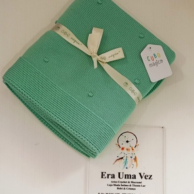 Manta verde de malha com fita e etiqueta com texto Cubo mágico, sobre placa com texto Era Uma Vez