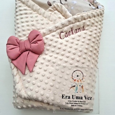 Manta bege com textura bolinhas, laço cor-de-rosa e bordado Caetana, cartão com texto Era Uma Vez em fundo branco