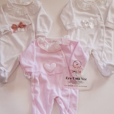 Três macacões de bebé em rosa e branco com colarinhos rendados e laços.