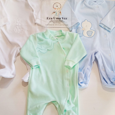 Três pijamas de bebé coloridos, branco, verde água e azul, com bordados e aplicações, sobre fundo claro