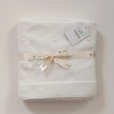 Manta branca de tecido tricotado com pequenos detalhes em relevo e etiqueta CUBO mágico