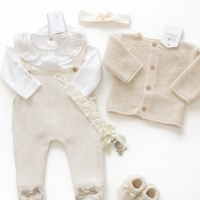 Conjunto de roupa de bebé bege e branco com body, jardineiras, cardigã, botins e faixa de cabeça