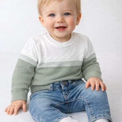 Bebé com camisola branca e verde claro e calças de ganga azuis sentado