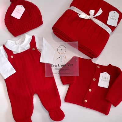 Conjunto vermelho para bebé com gorro, casaco, jardineira, camisola branca e manta trançada.