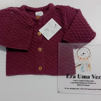 Camisola de bebé em malha vinho com botões de madeira e etiqueta, sobre fundo branco com cartão Era Uma Vez